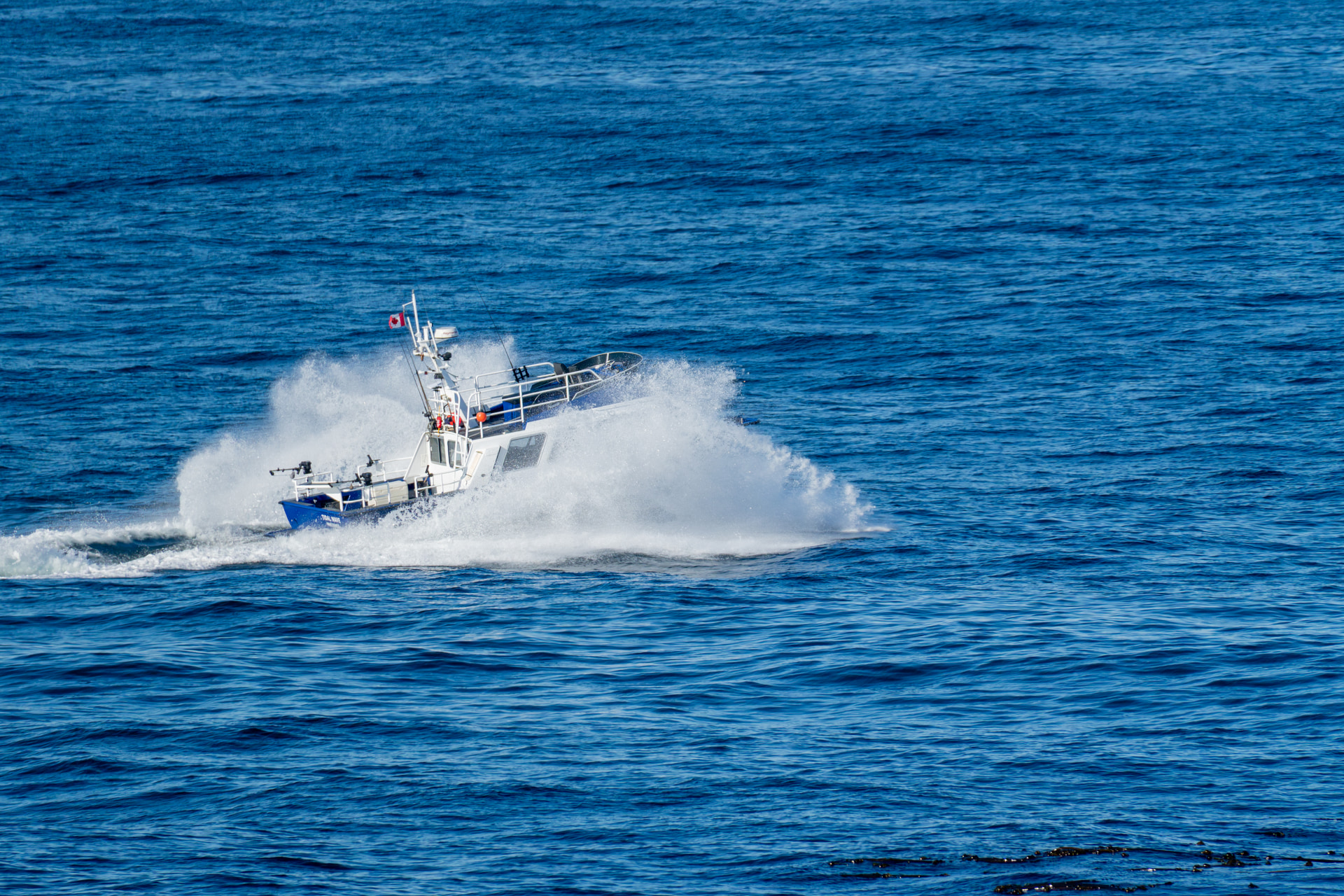 Kleines blaues Arbeitsboot fährt mit hoher Gischt durch die Wellen vor Ucluelet